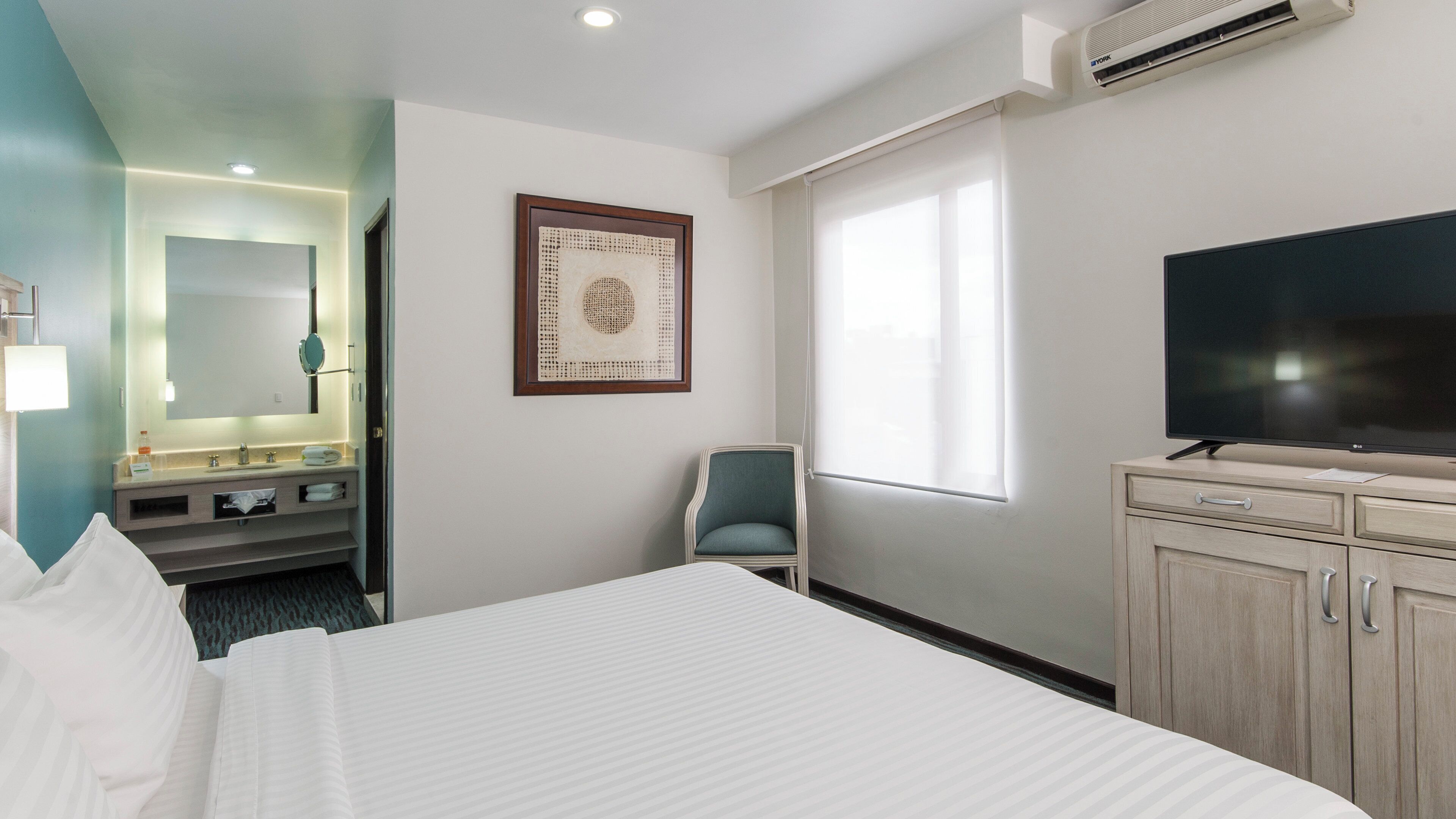 A hotel room with a bed, a television, a chair, a desk, and a window.