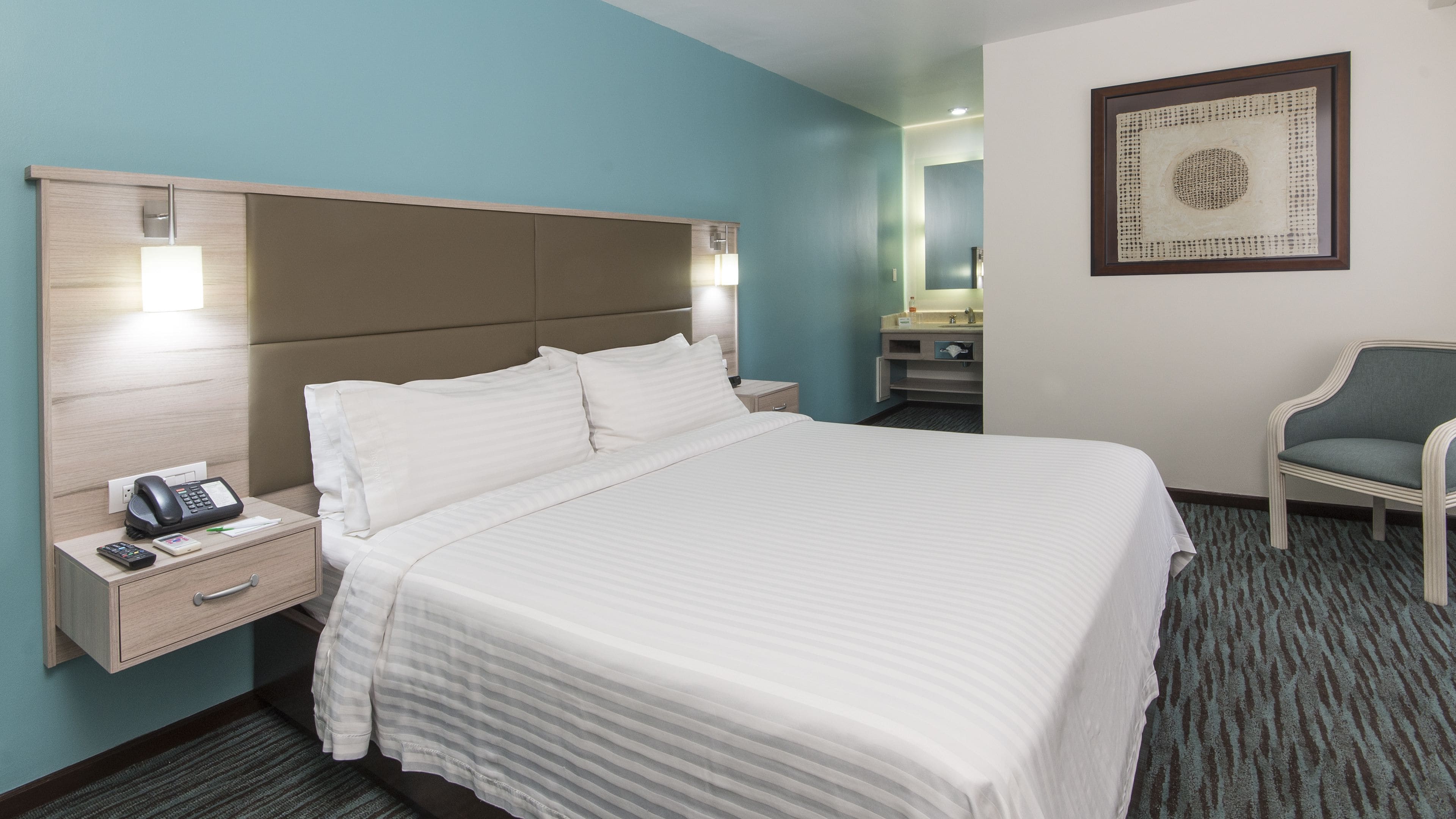 Une chambre d’hôtel avec un grand lit, des tables de chevet, un bureau, une chaise et une salle de bain visible au fond.