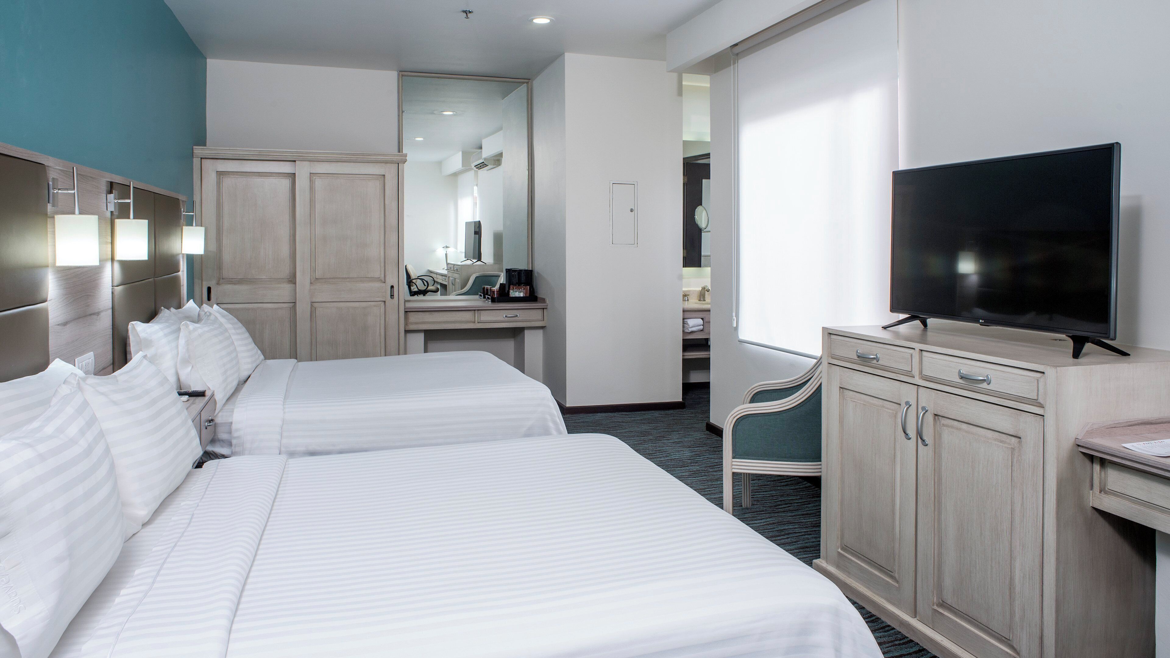 A hotel room with two beds, a desk, a television, and a mirror.