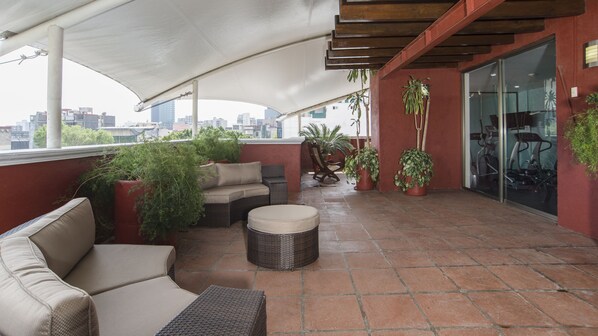 A covered outdoor seating area with wicker furniture, potted plants, and a view of the cityscape. - Holiday Inn & Suites Mexico Zona Reforma by IHG (Mexico City)