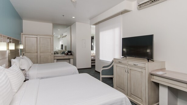 Quarto de hotel com duas camas, uma escrivaninha, uma televisão e um espelho.