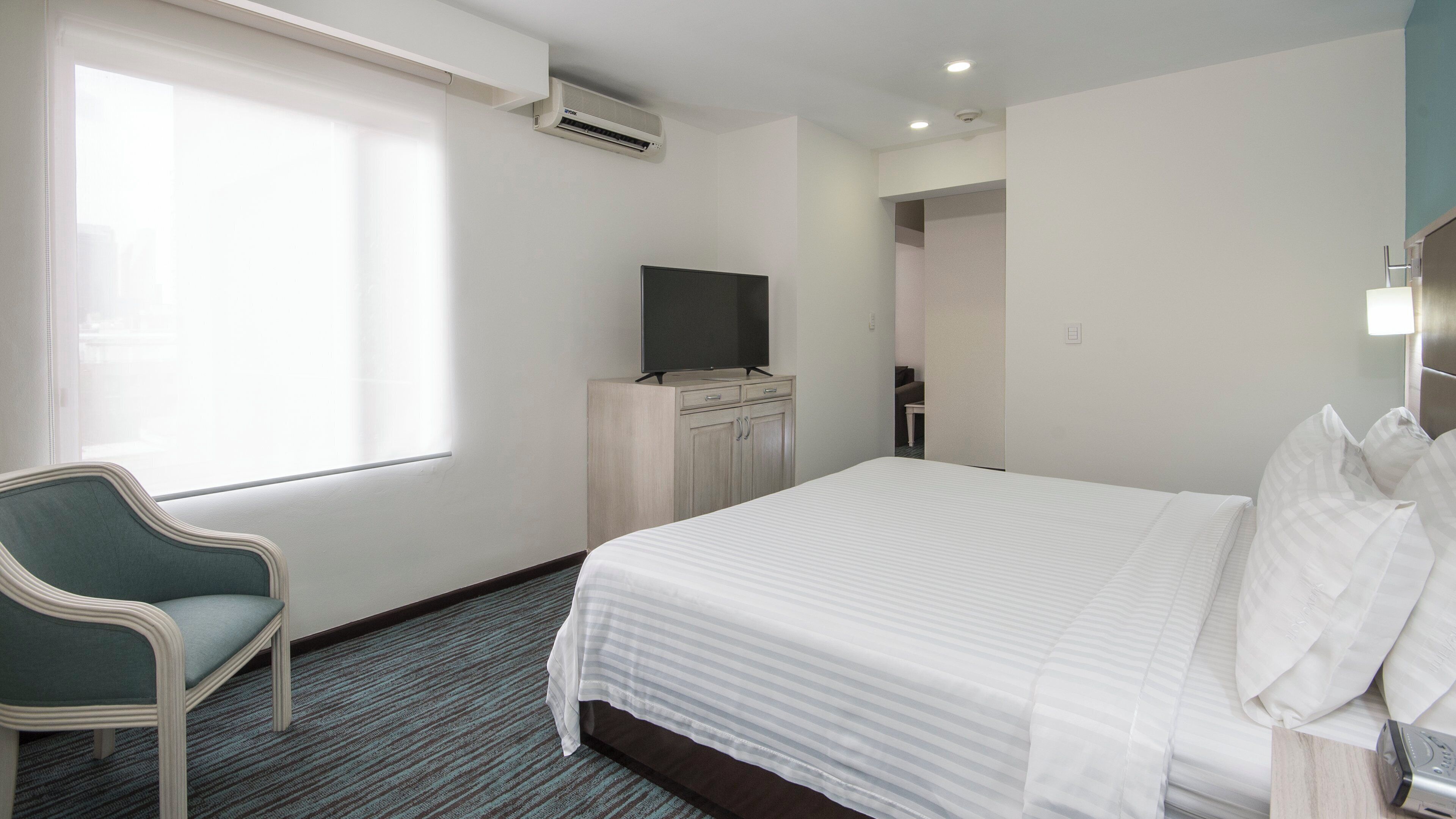 Une chambre d’hôtel avec un lit, un téléviseur posé sur un meuble, une chaise et une fenêtre.