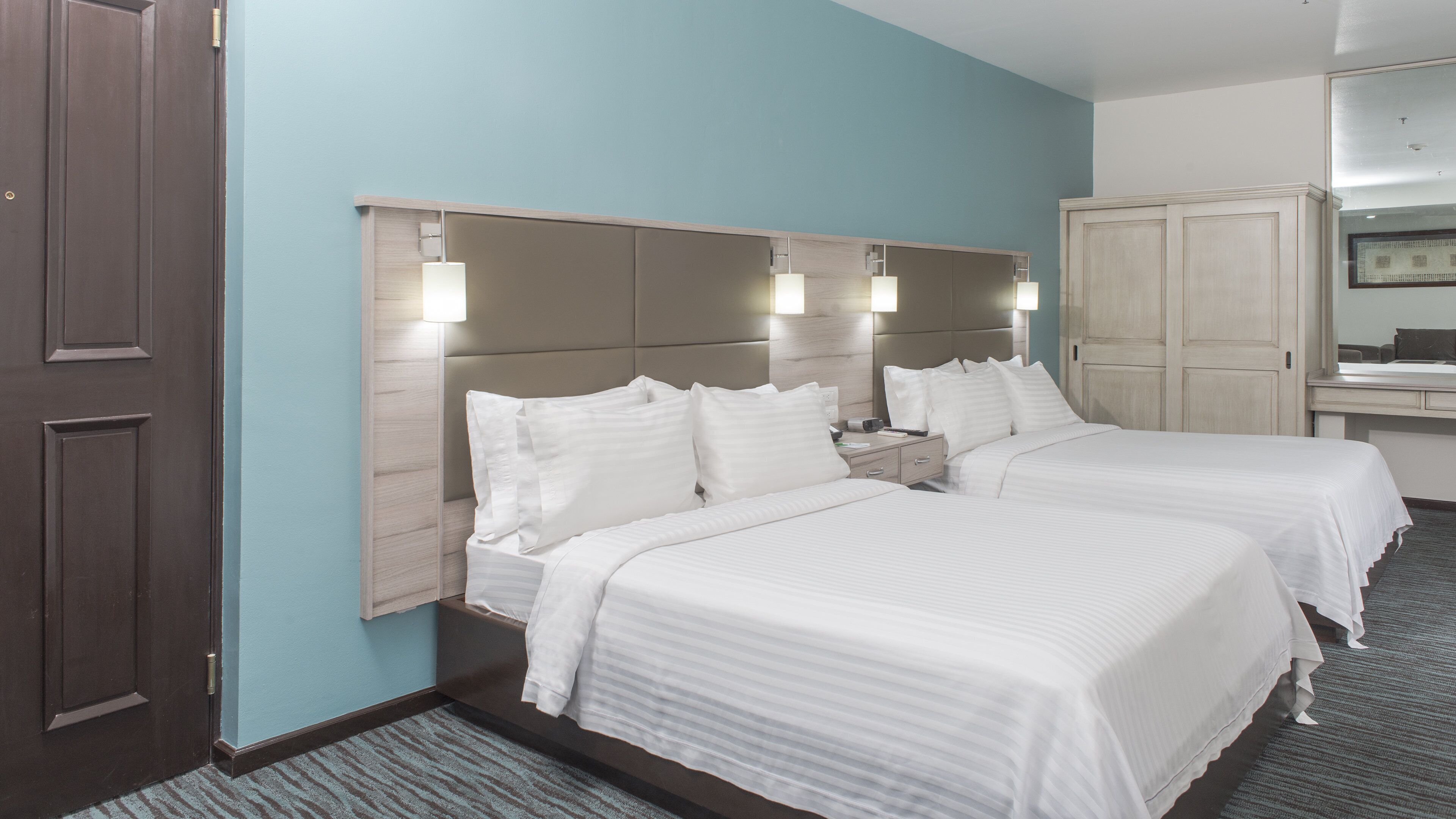 A hotel room with two beds, a nightstand, a lamp, and a mirror.