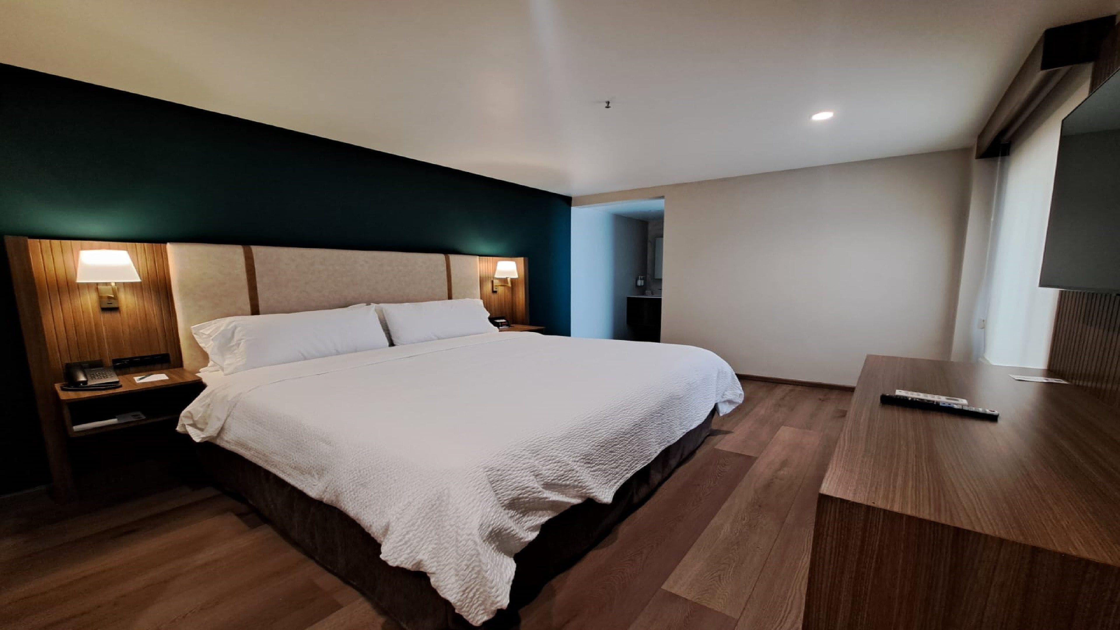 A hotel room with a large bed, bedside tables with lamps, a wooden desk, and a television.