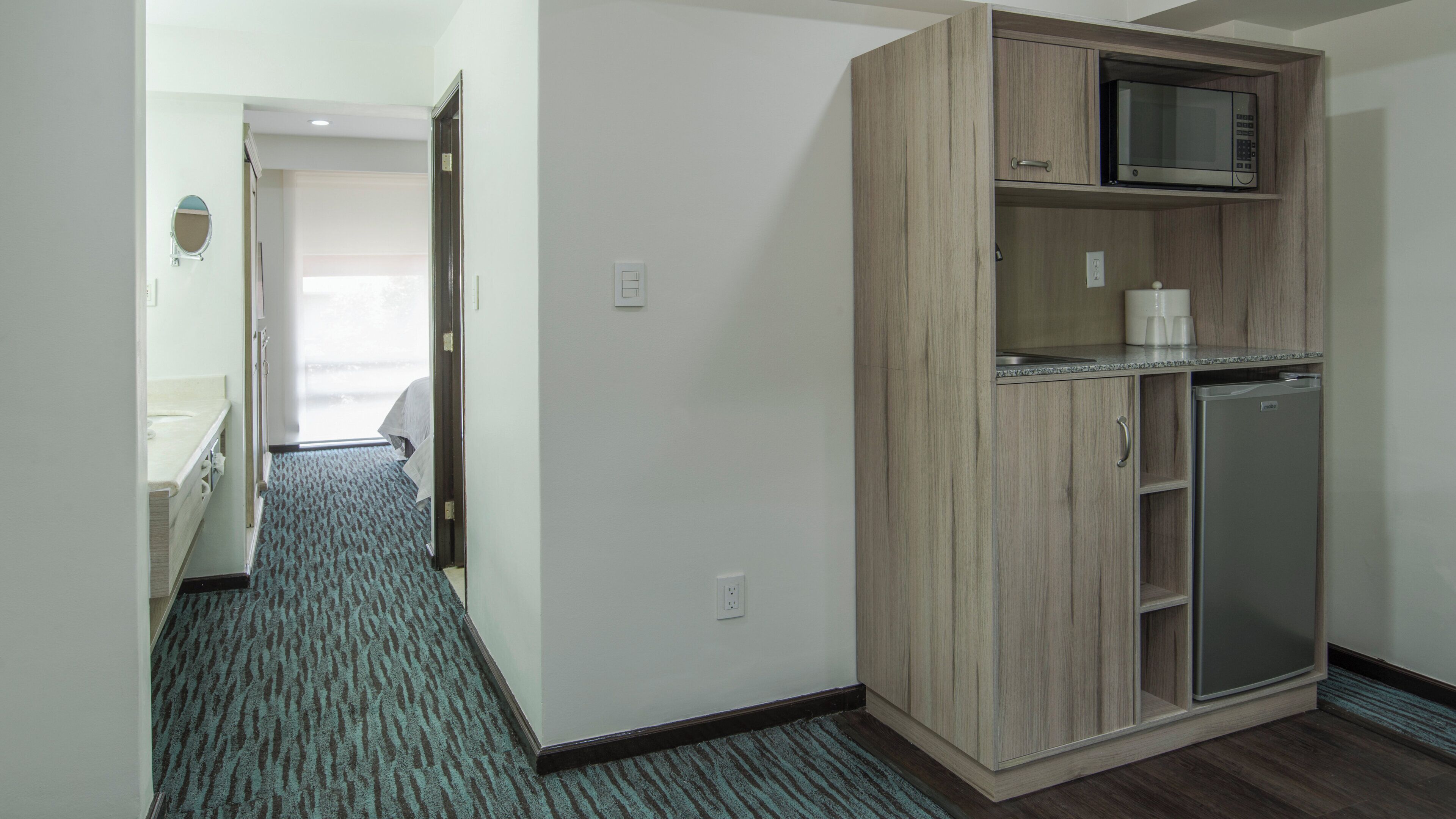 A hotel room with a kitchenette, a microwave, and a refrigerator.