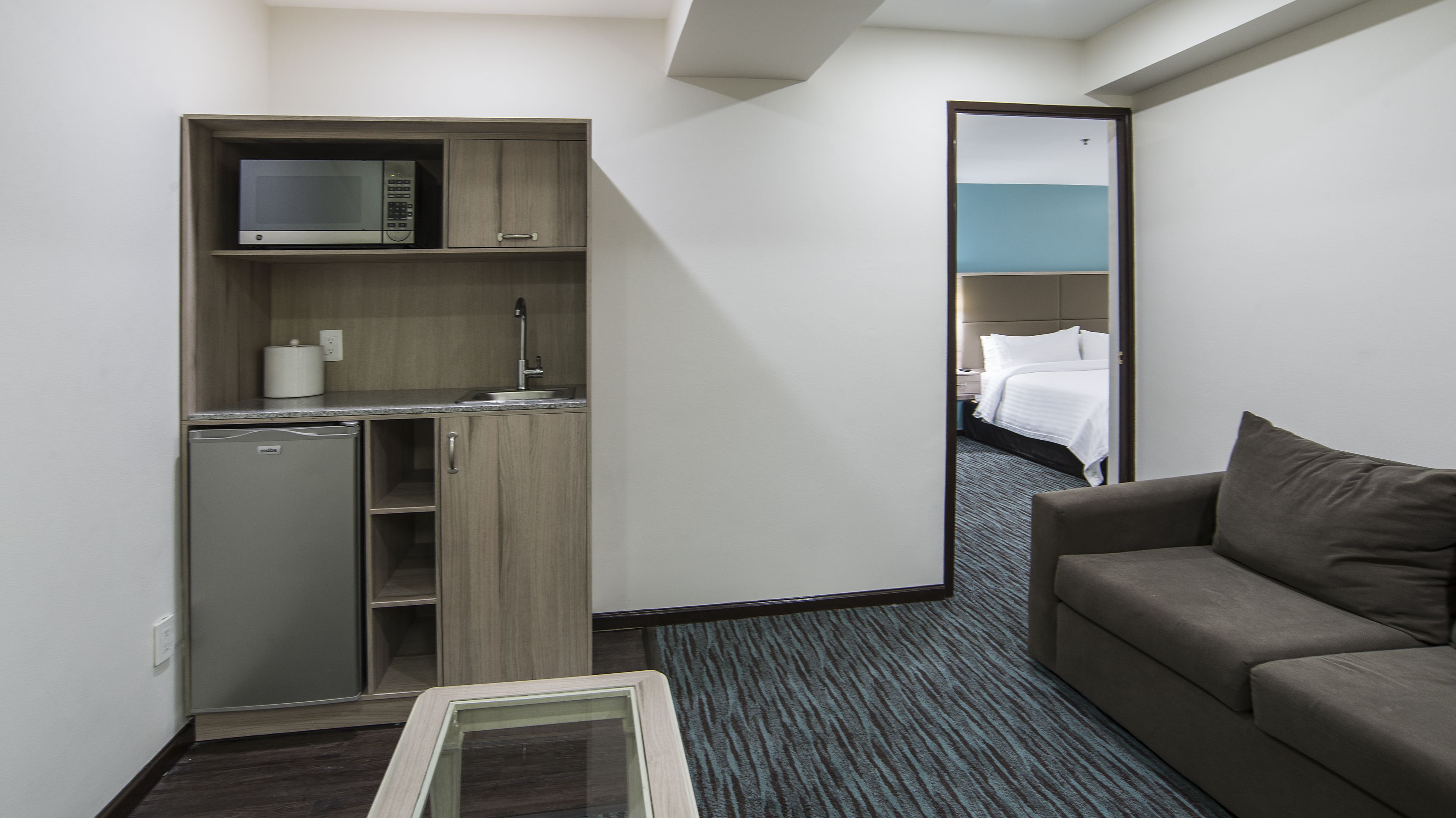 A compact hotel room with a kitchenette, a bed, and a sofa.