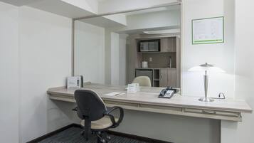 A hotel room with a desk, chair, telephone, lamp, and a mirror.