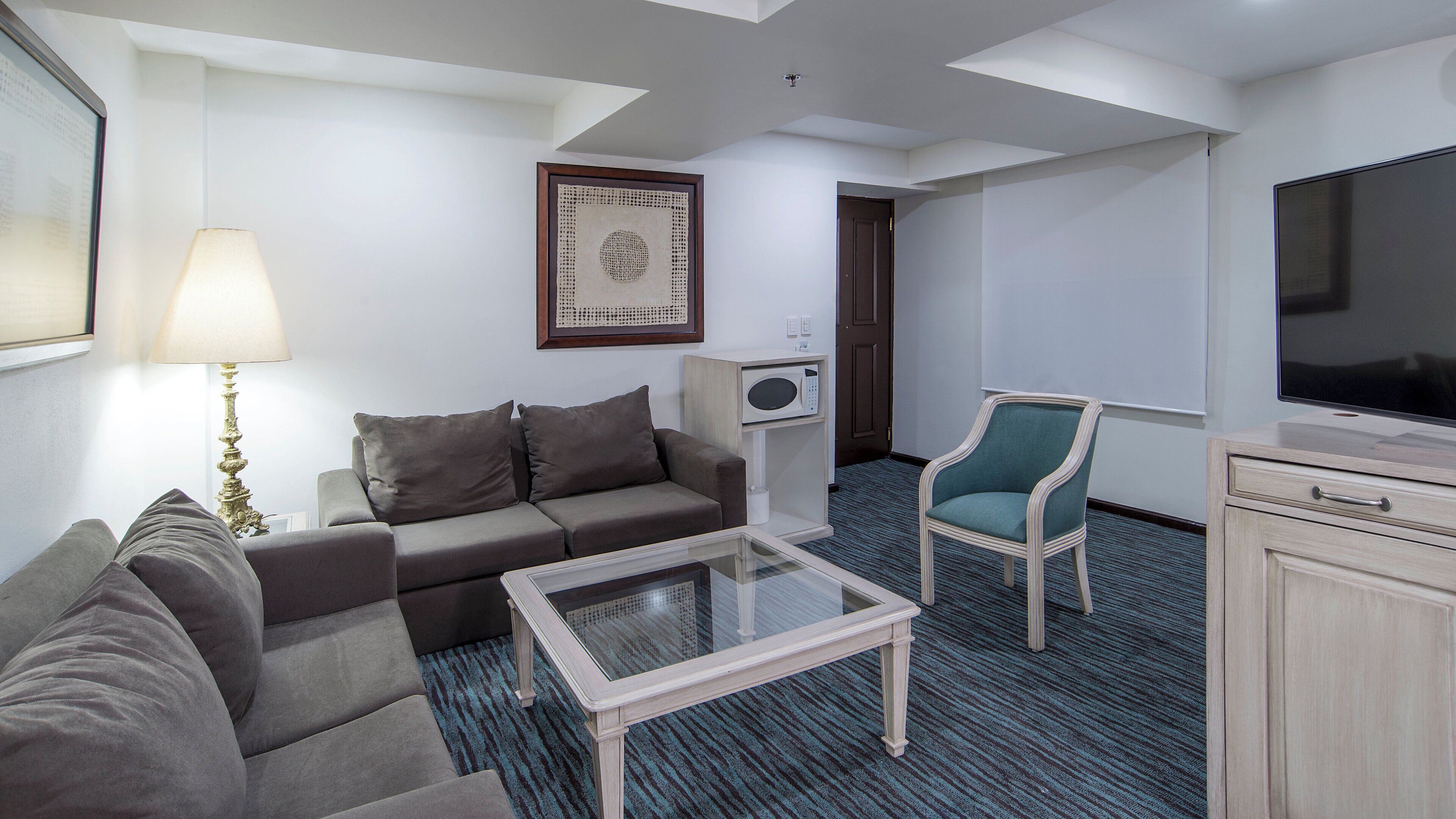 Een hotelkamer met een bank, een kleine tafel, een televisie, een magnetron en een stoel.