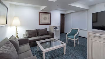 Une chambre d’hôtel équipée d’un canapé, d’une petite table, d’une télévision, d’un four à micro-ondes et d’une chaise.
