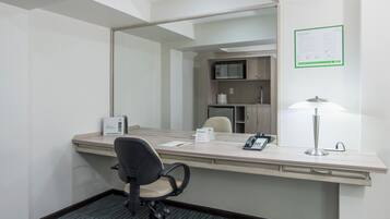 A hotel room with a desk, chair, telephone, lamp, and a mirror.