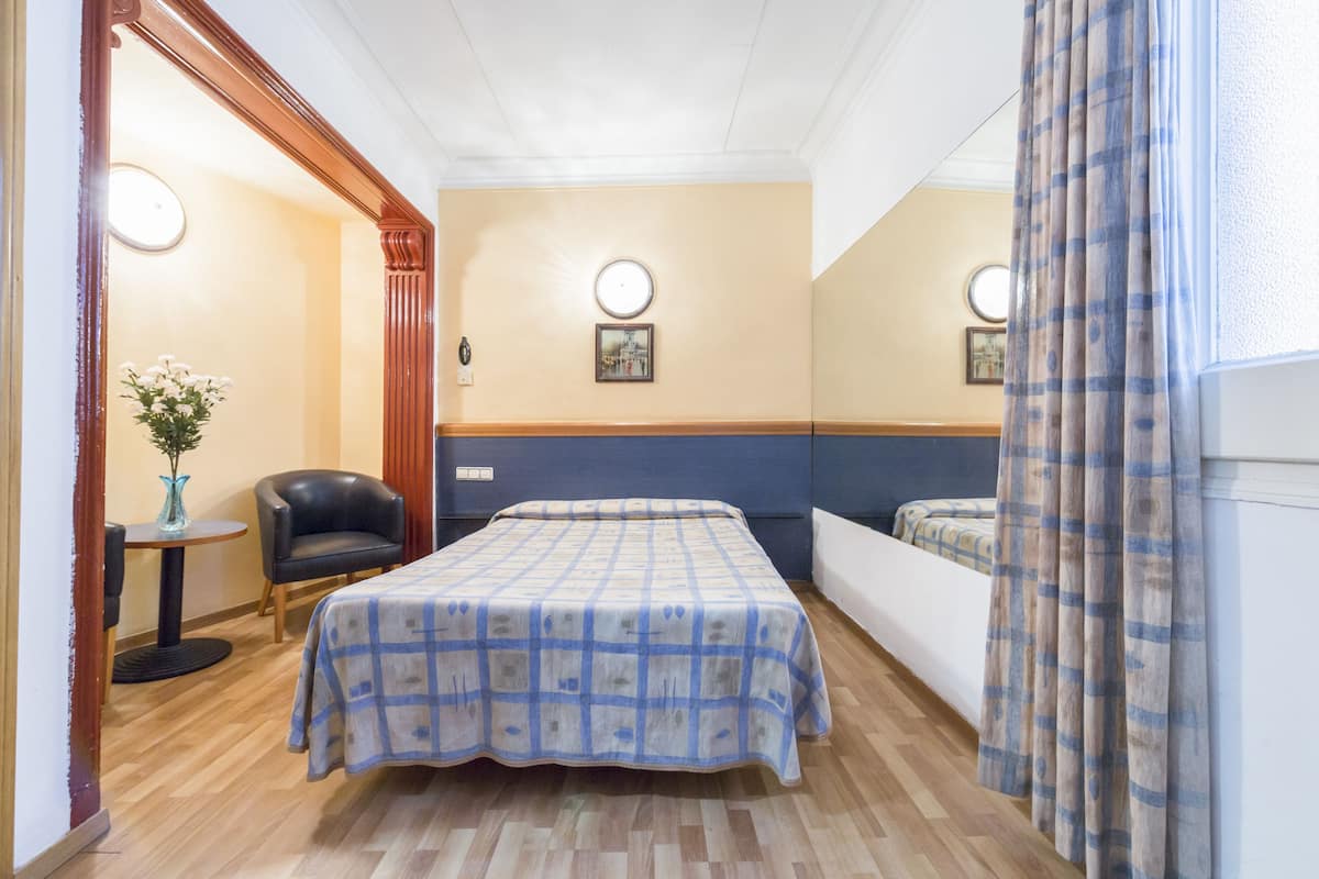 Ein Hotelzimmer mit einem Bett, einem Sessel, einem kleinen Tisch mit einer Vase und zwei Wandleuchten.