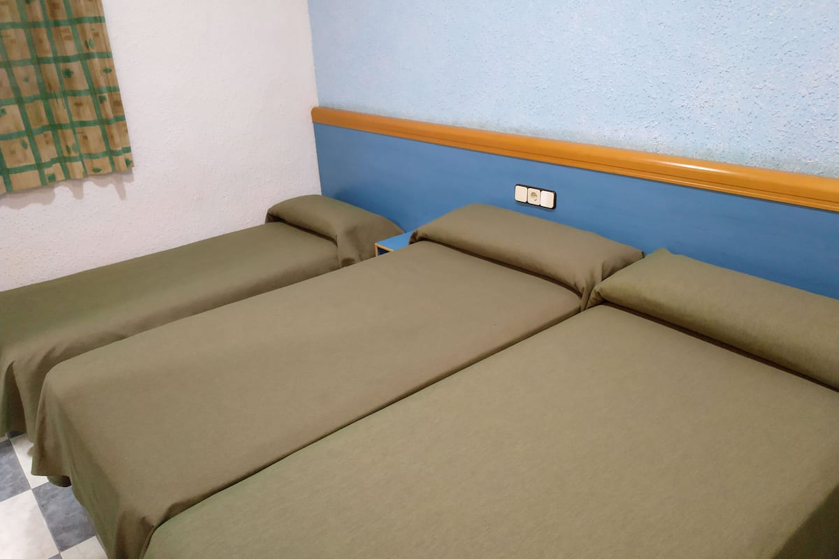 Ein Zimmer mit zwei Einzelbetten, einem kleinen Tisch und einer Steckdose.