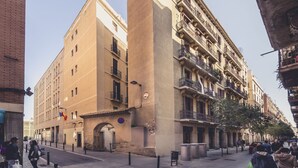 A street view with a tall, beige building with balconies and a smaller adjacent building.
