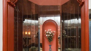 A room with a checkered floor, a wooden-framed glass partition, and a vase with flowers on a small table.