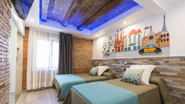 A hotel room with two beds, a brick wall, a mural of a cityscape, and a skylight.