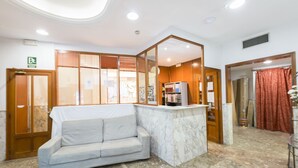 A lobby with a marble reception desk, a grey sofa, wooden doors, and a red curtain.