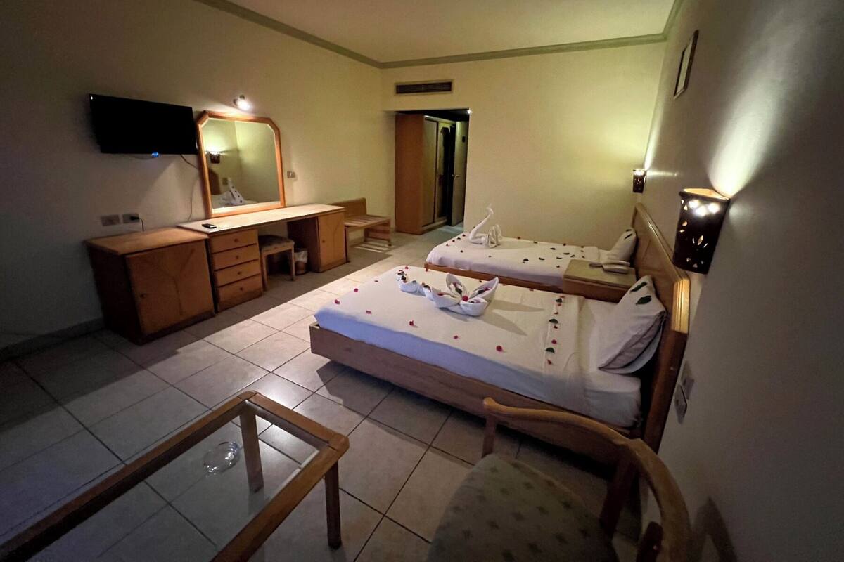 Habitación de hotel con dos camas, un escritorio, una silla, un televisor y un espejo.
