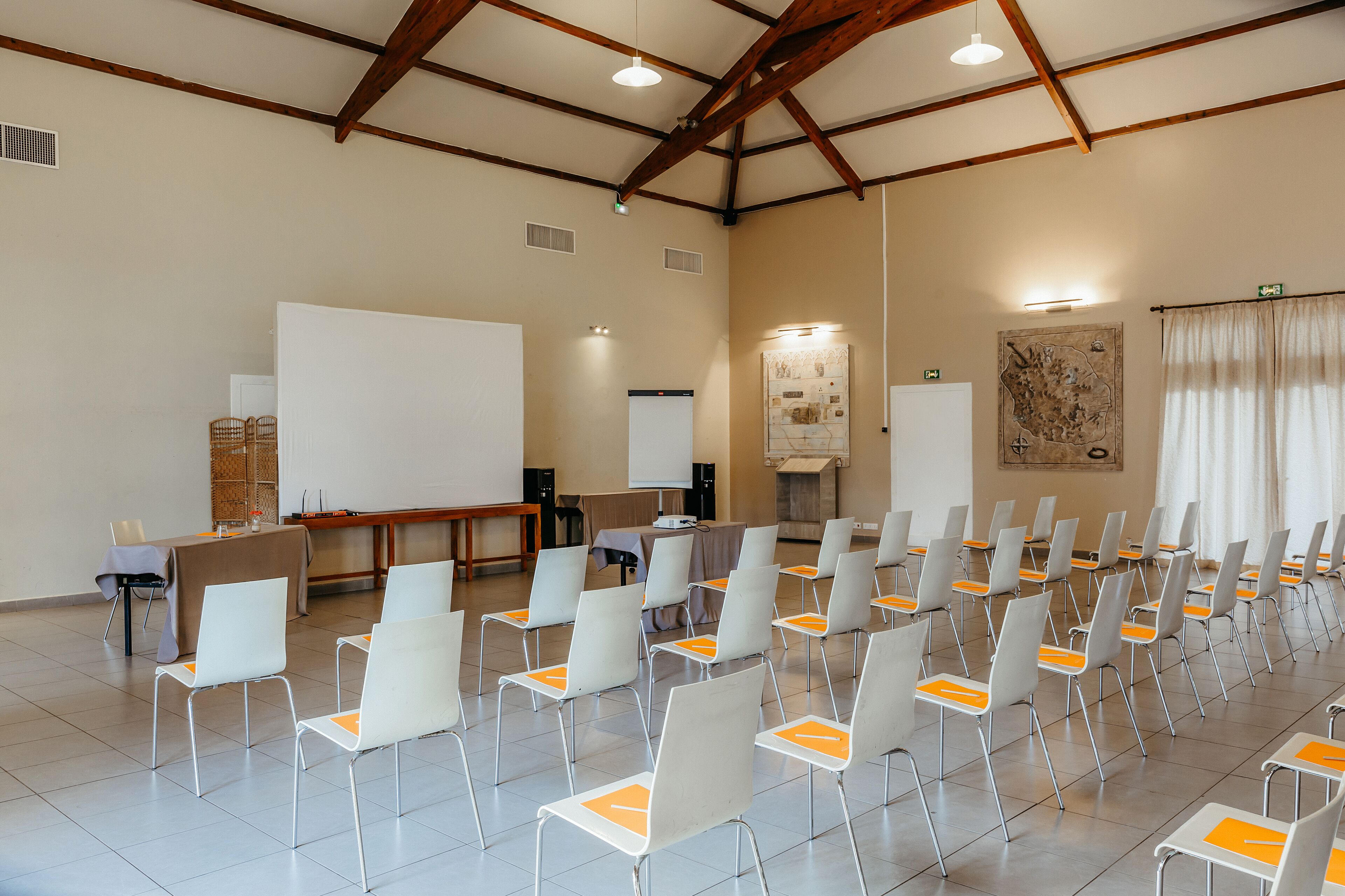 A conference room with rows of white chairs, a whiteboard, and a projector screen.