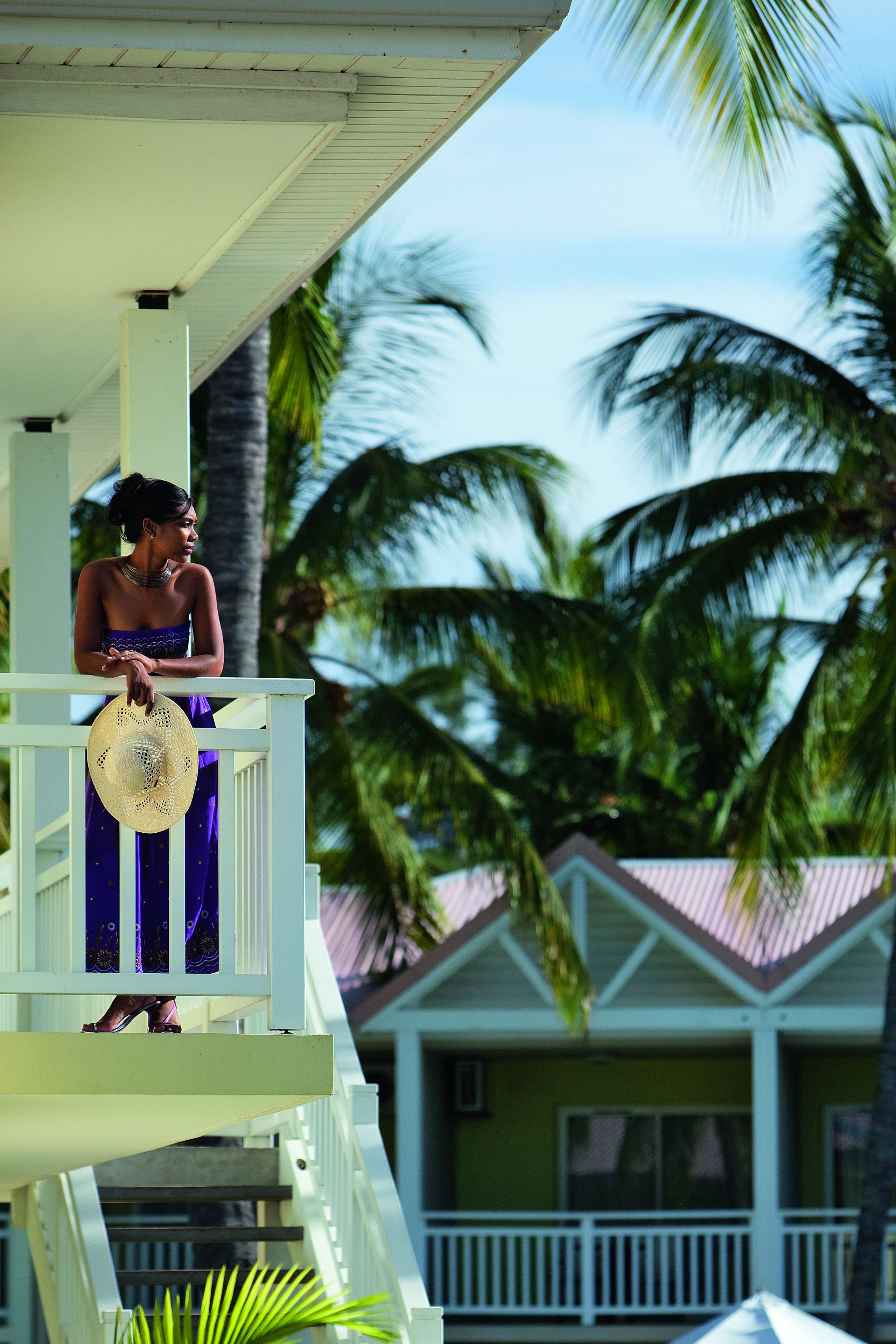 A person on a balcony with a view of palm trees and a building with a red roof.