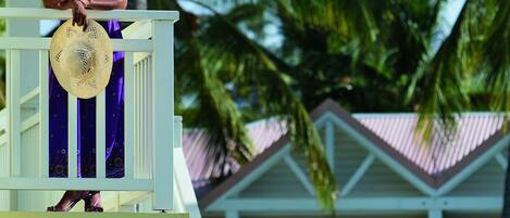 A person on a balcony with a view of palm trees and a building with a red roof.