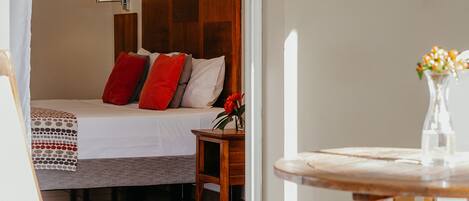 A hotel room with a bed, a wooden headboard, a nightstand, a table with a vase of flowers, and a chair.