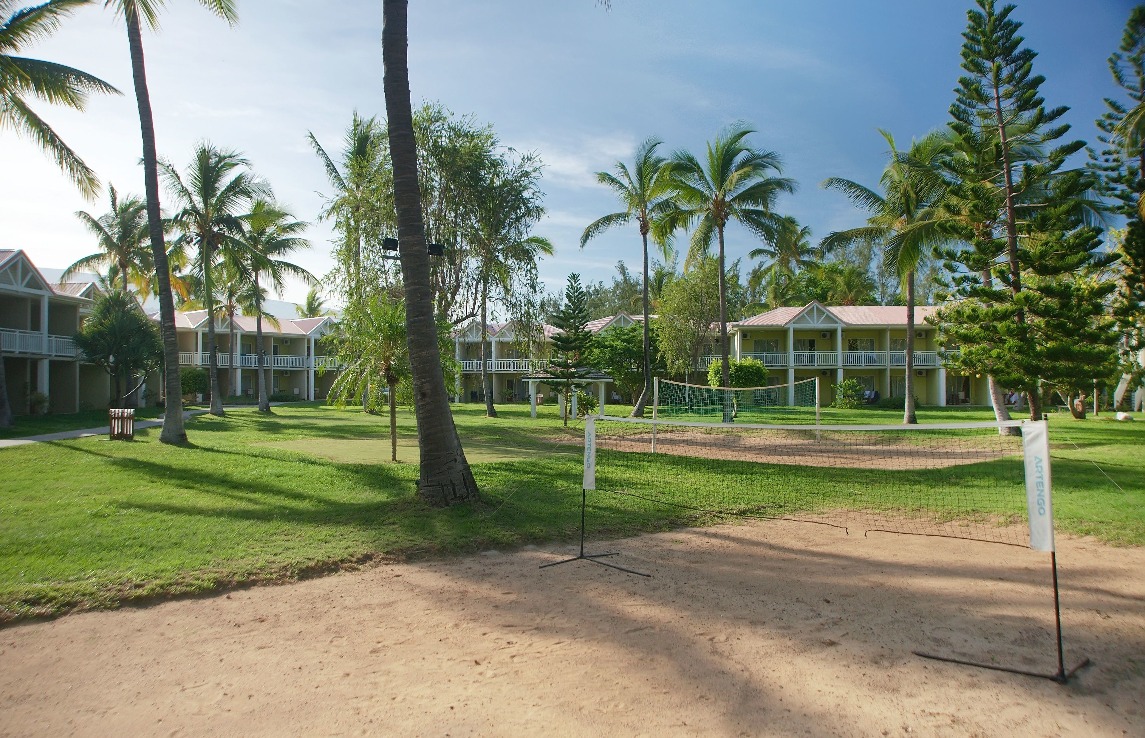 A sandy volleyball court surrounded by palm trees and a building with a balcony.