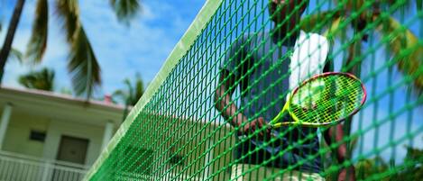 A tennis court with a net, palm trees, and a building in the background.