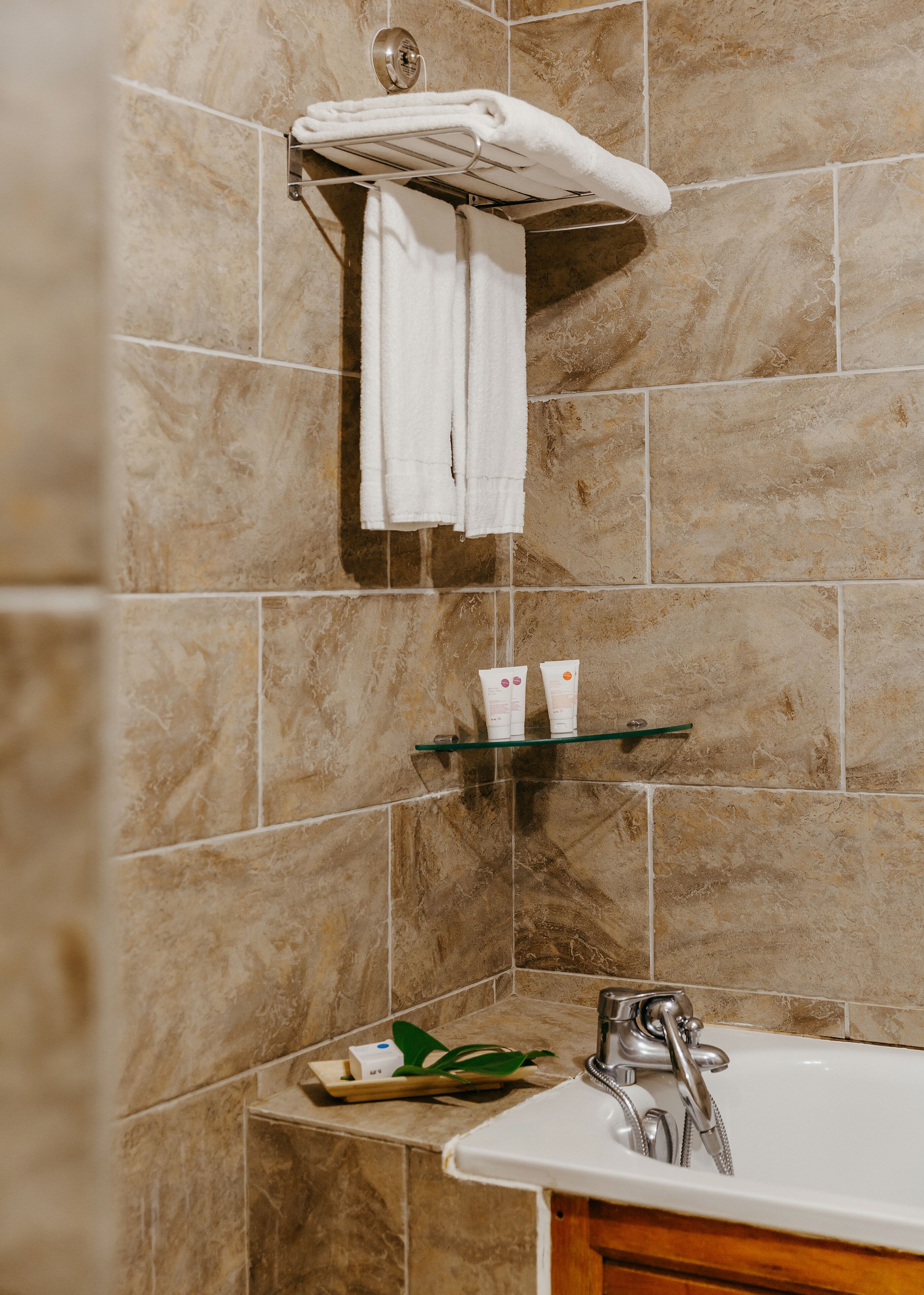 Ein Badezimmer mit beigen Fliesen, einem weißen Waschbecken, einem Handtuchhalter mit einem gefalteten Handtuch und einem Ablagebereich für Toilettenartikel.