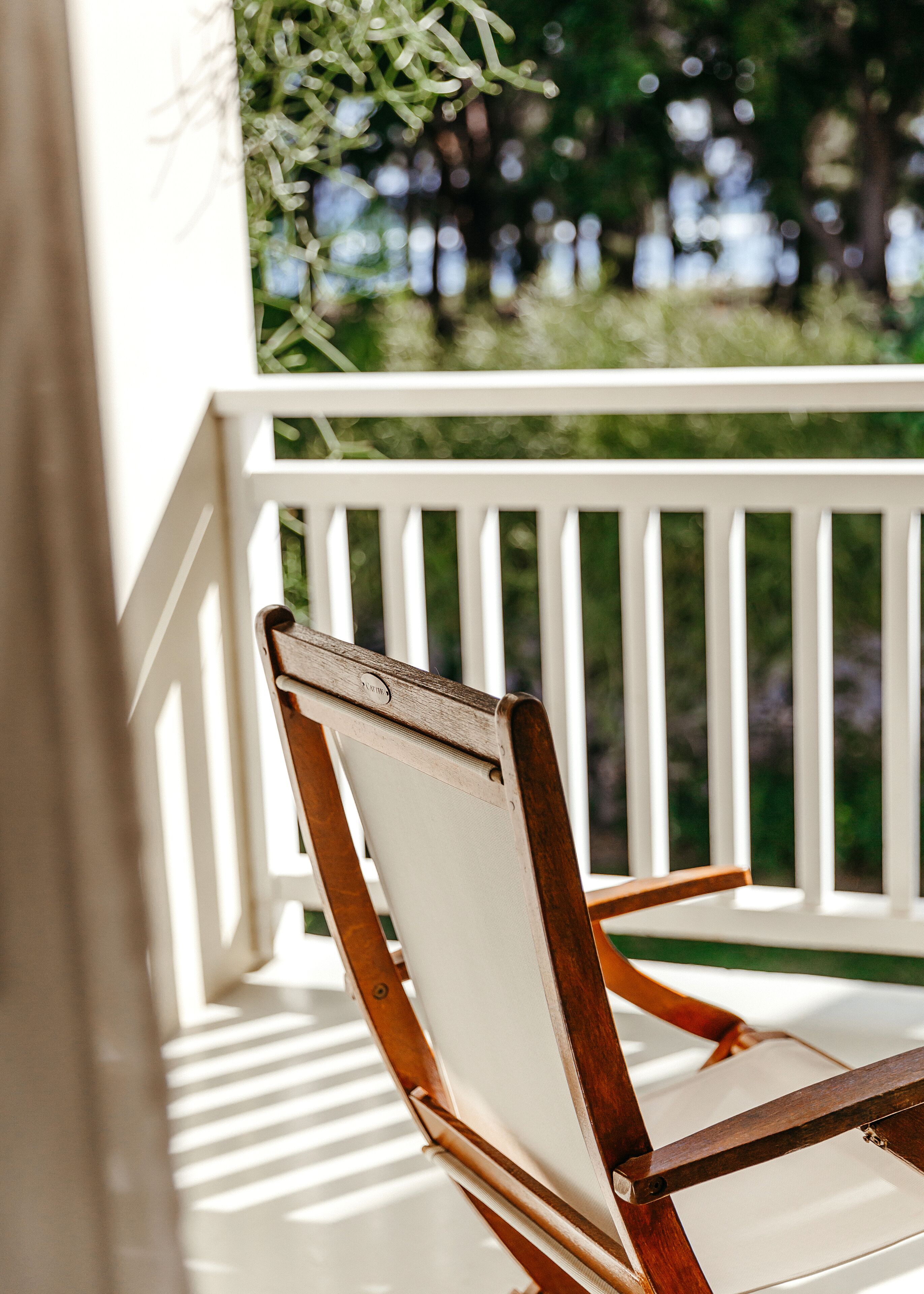 A wooden chair with a white cushion on a porch with white railings.