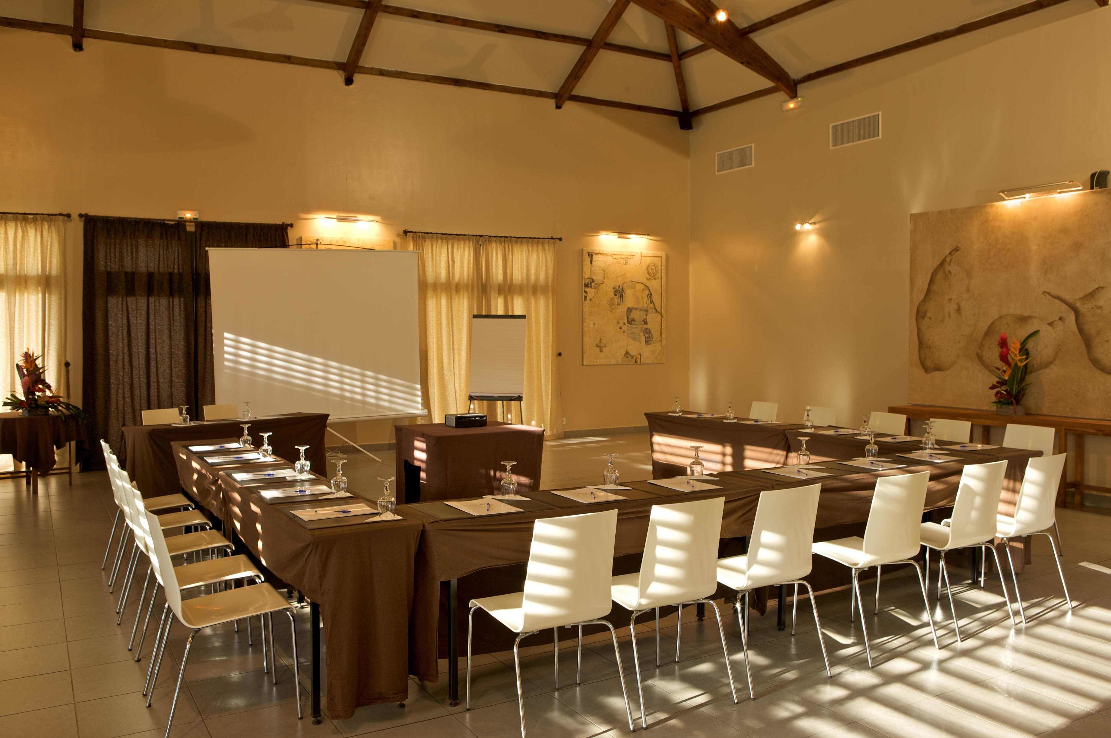 A conference room with a long table, white chairs, and a projector screen.