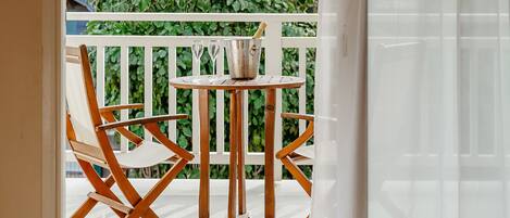 Una habitación con vistas a un balcón, una mesa con un cubo y vasos, y dos sillas de madera.