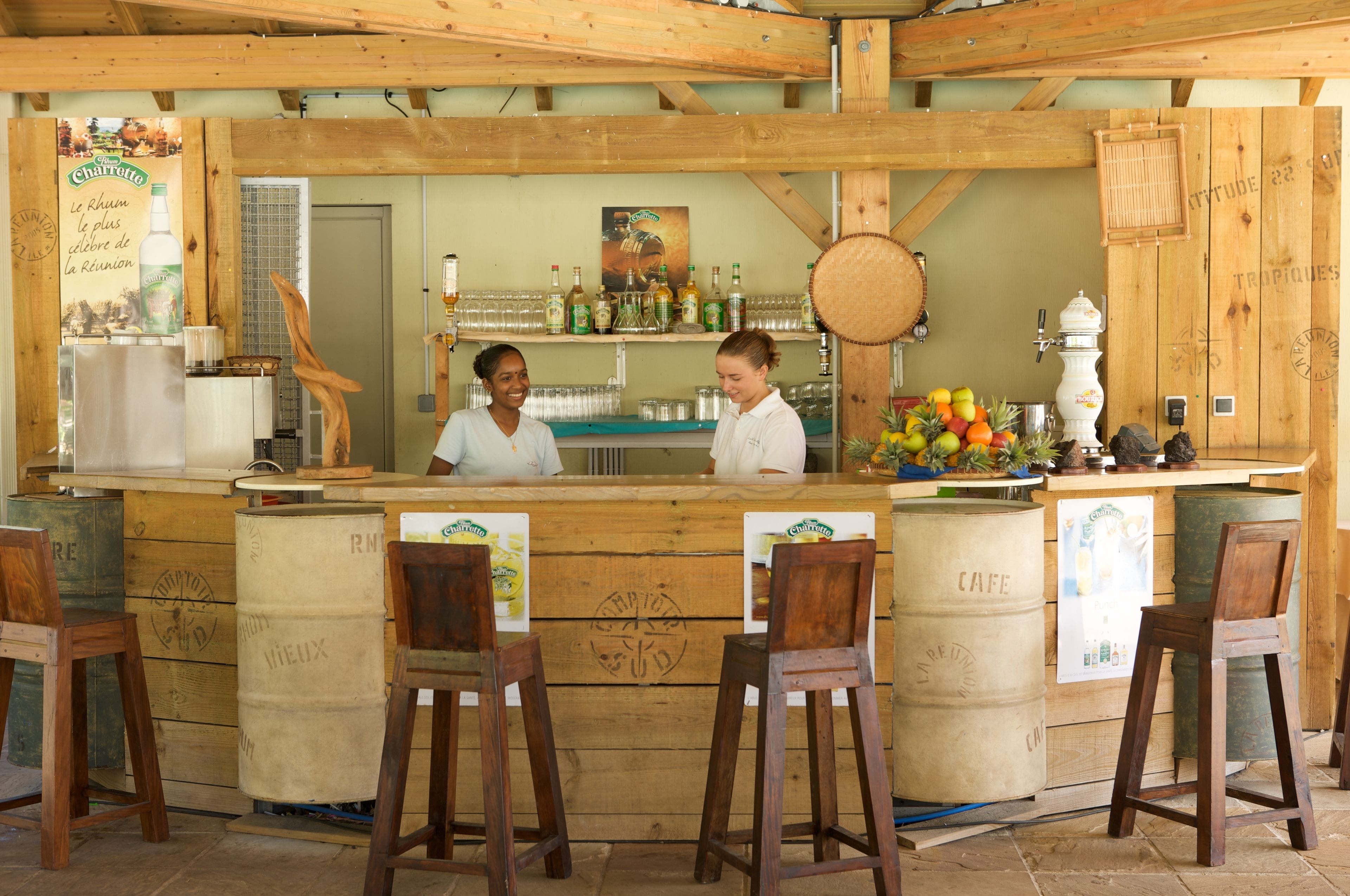 A rustic bar area with wooden beams, a counter with stools, and various bottles and glasses.