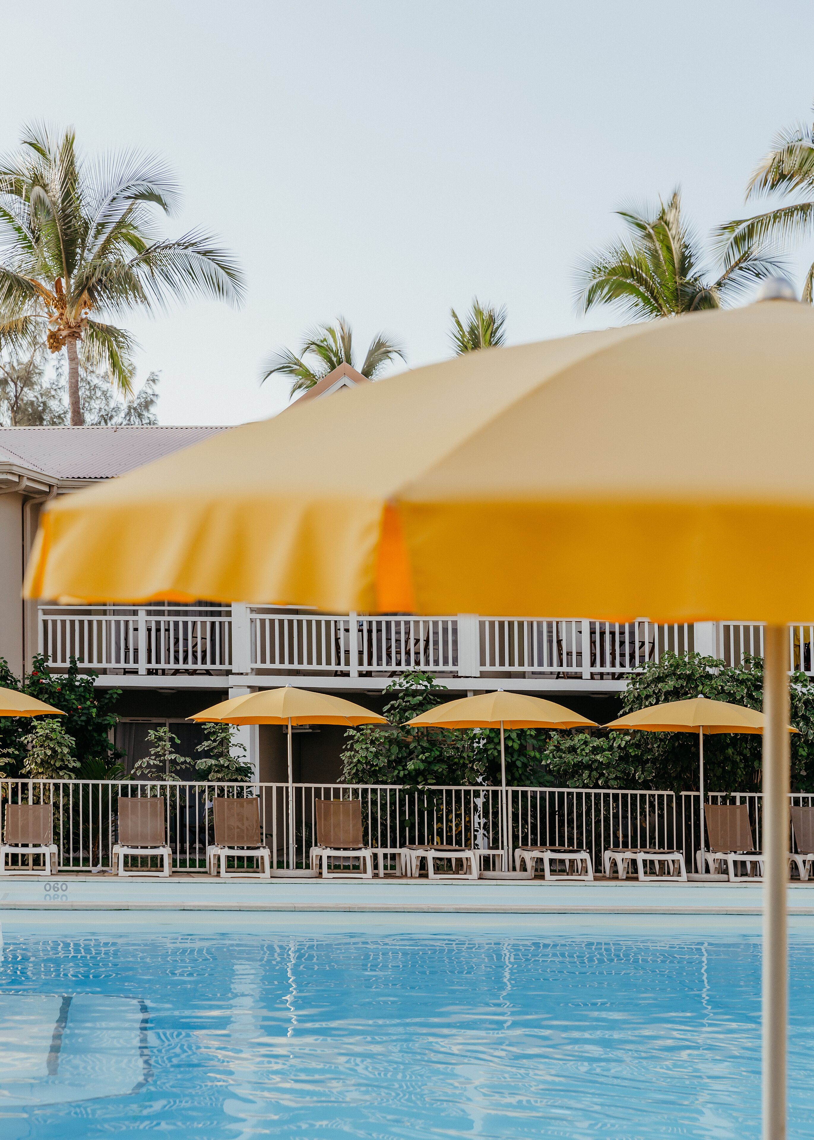 A pool area with yellow umbrellas, lounge chairs, and a building with balconies.
