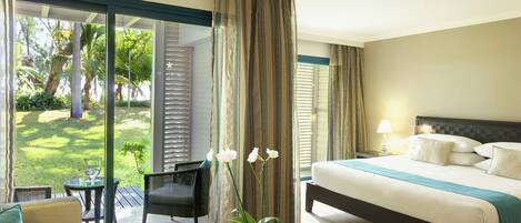 Quarto de hotel com cama, uma mesinha, uma cadeira e vista para um jardim através de uma porta deslizante.