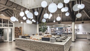 A modern kitchen with a central island, hanging spherical pendant lights, and a variety of food items displayed on the island. - LUX* Saint Gilles (Saint-Paul)