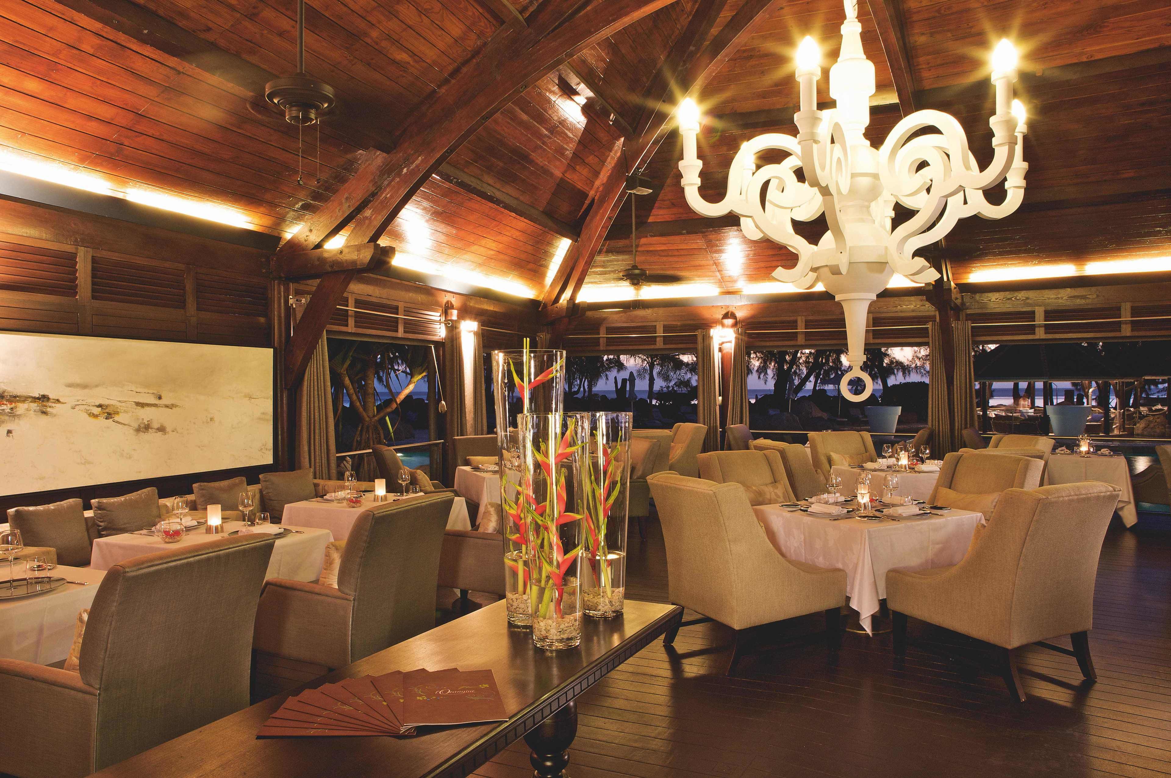 A restaurant with wooden ceiling beams, chandeliers, and tables set for dining.