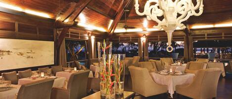 Un restaurante con vigas de madera en el techo, candelabros y mesas dispuestas para comer.