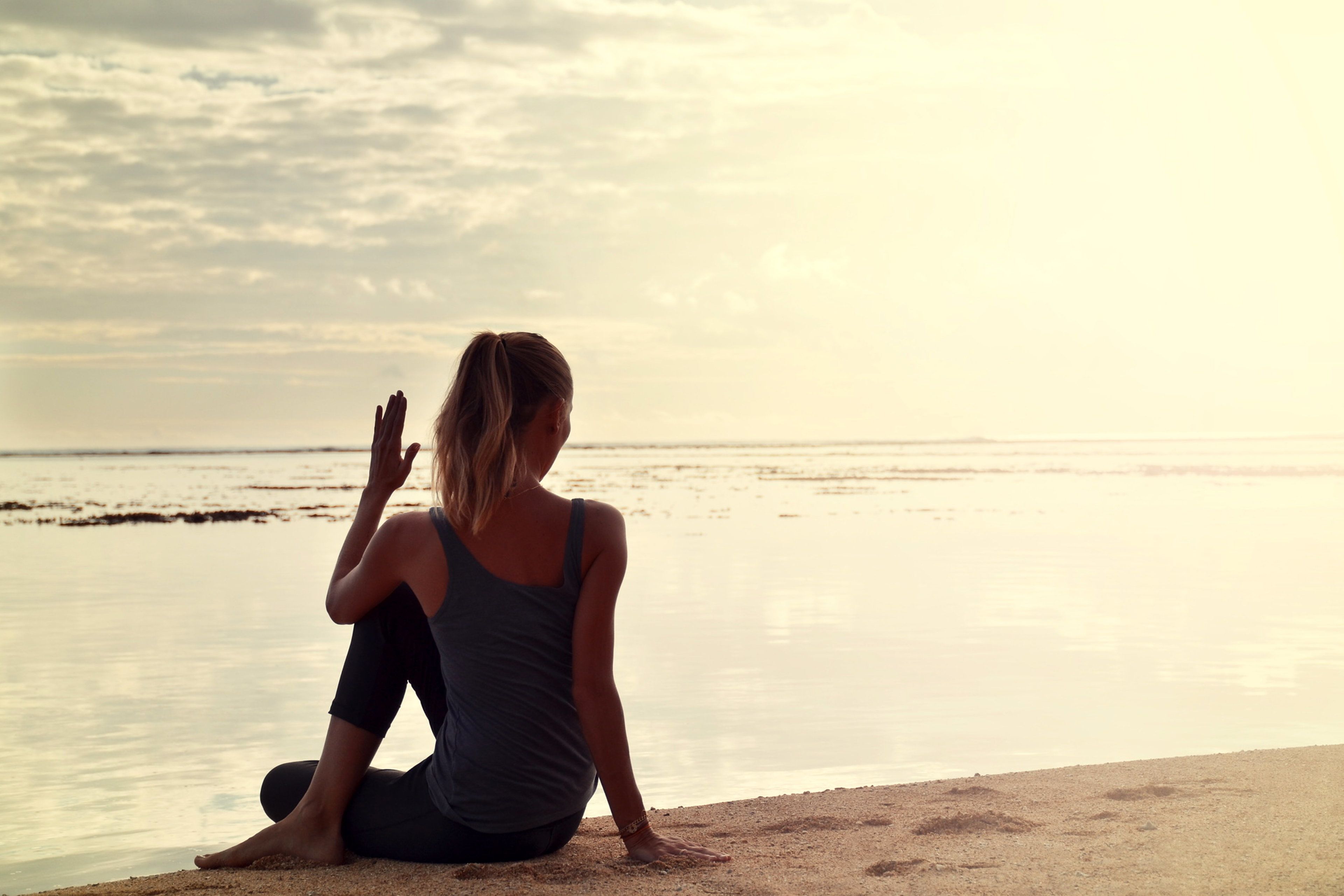 Una persona sentada en una playa arenosa mirando al océano durante el atardecer.