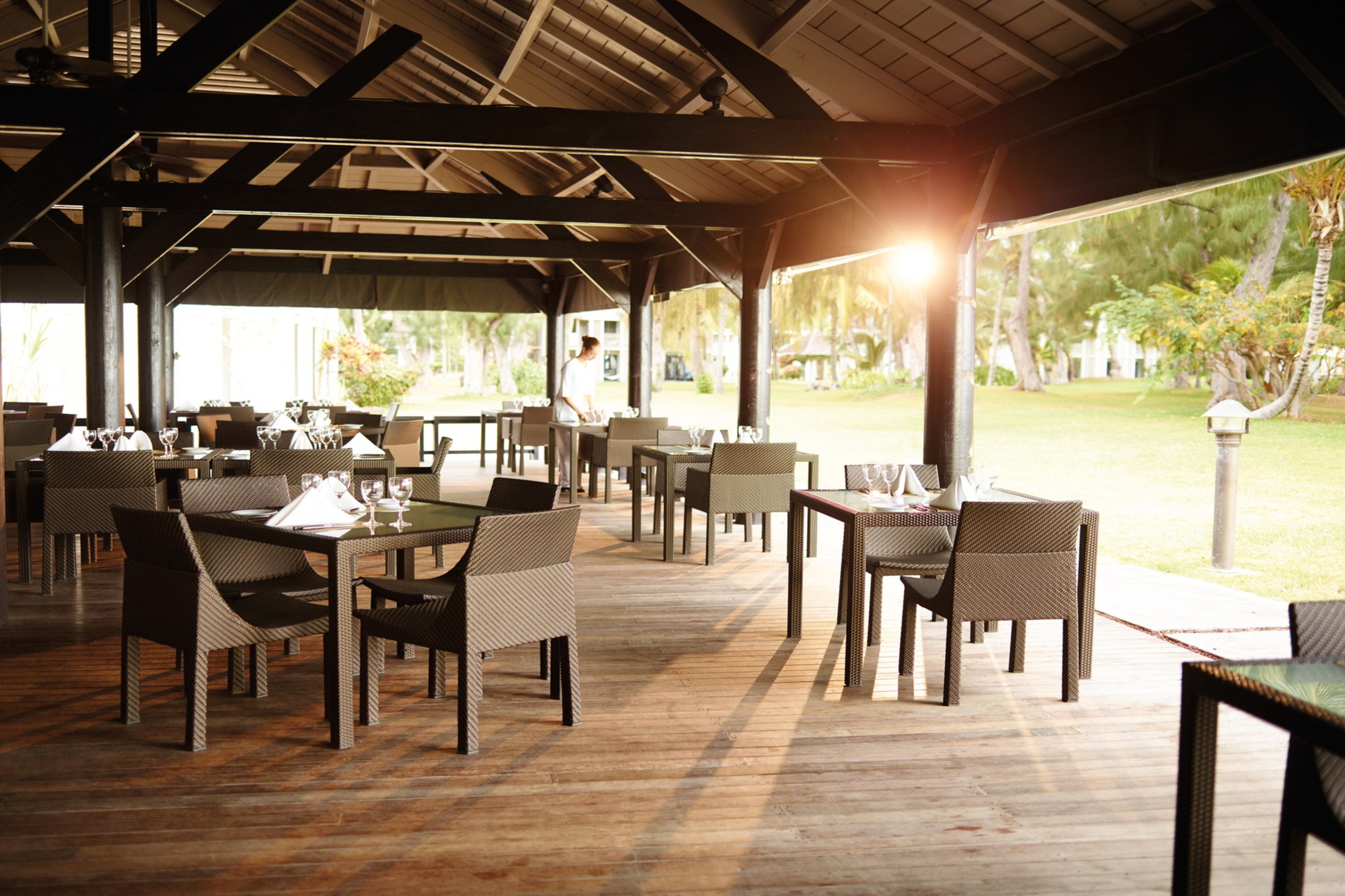 A covered outdoor dining area with wicker furniture and tables set for guests.
