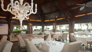A restaurant with outdoor seating, a pool view, and a chandelier. - LUX* Saint Gilles (Saint-Paul)
