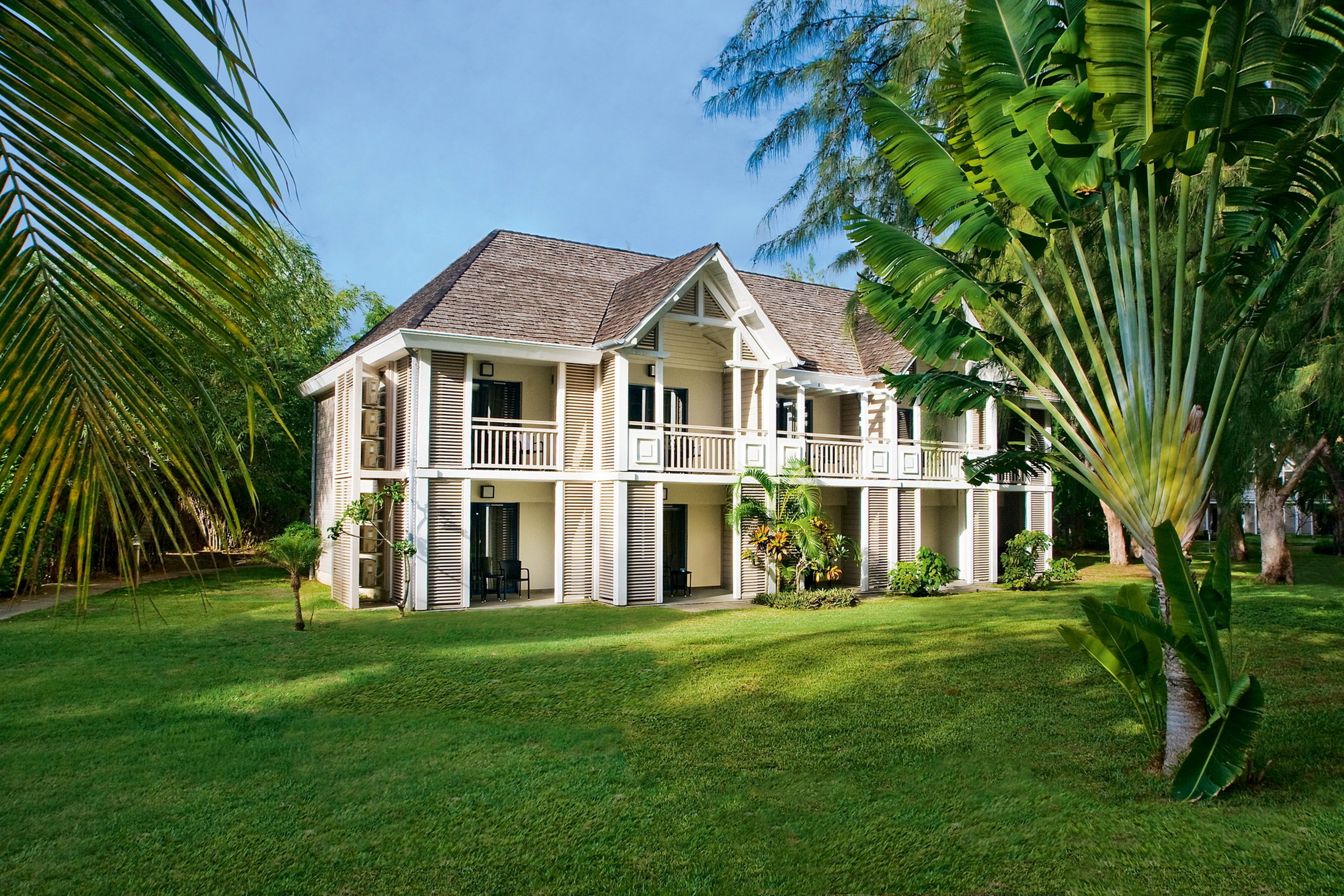 A two-story building with a balcony, surrounded by lush greenery and palm trees.