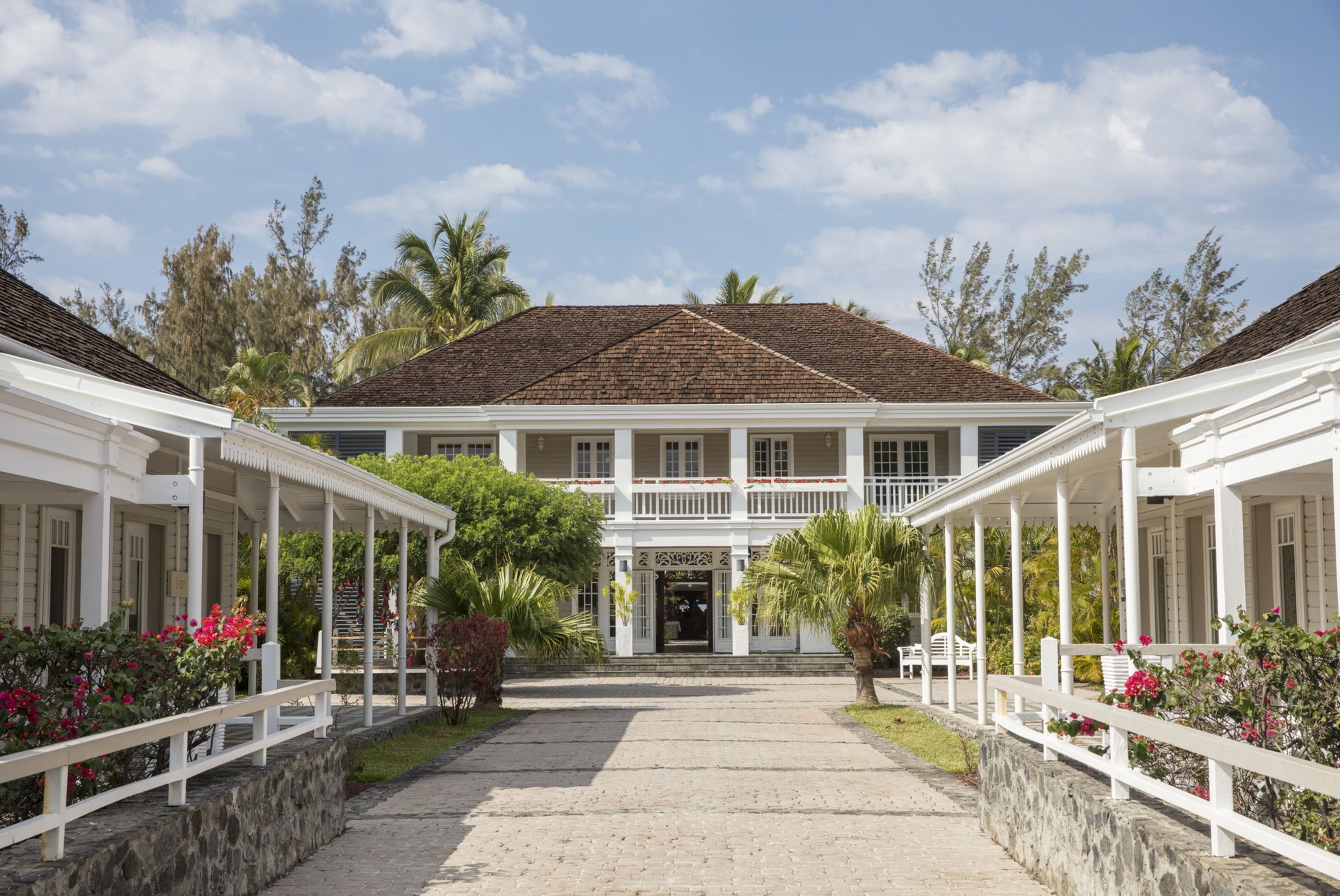 A colonial-style building with a central entrance, white columns, and a covered walkway on either side.