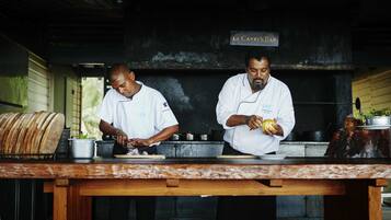 Two chefs preparing food at Le Carry's Bar, with a wooden table and kitchen equipment visible.