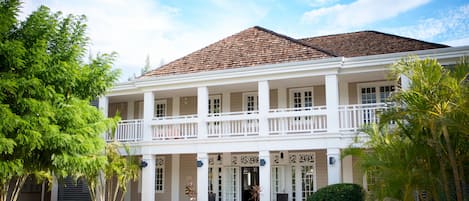 Un edificio de estilo colonial de dos pisos, con un balcón, ventanas amplias y fachada simétrica.
