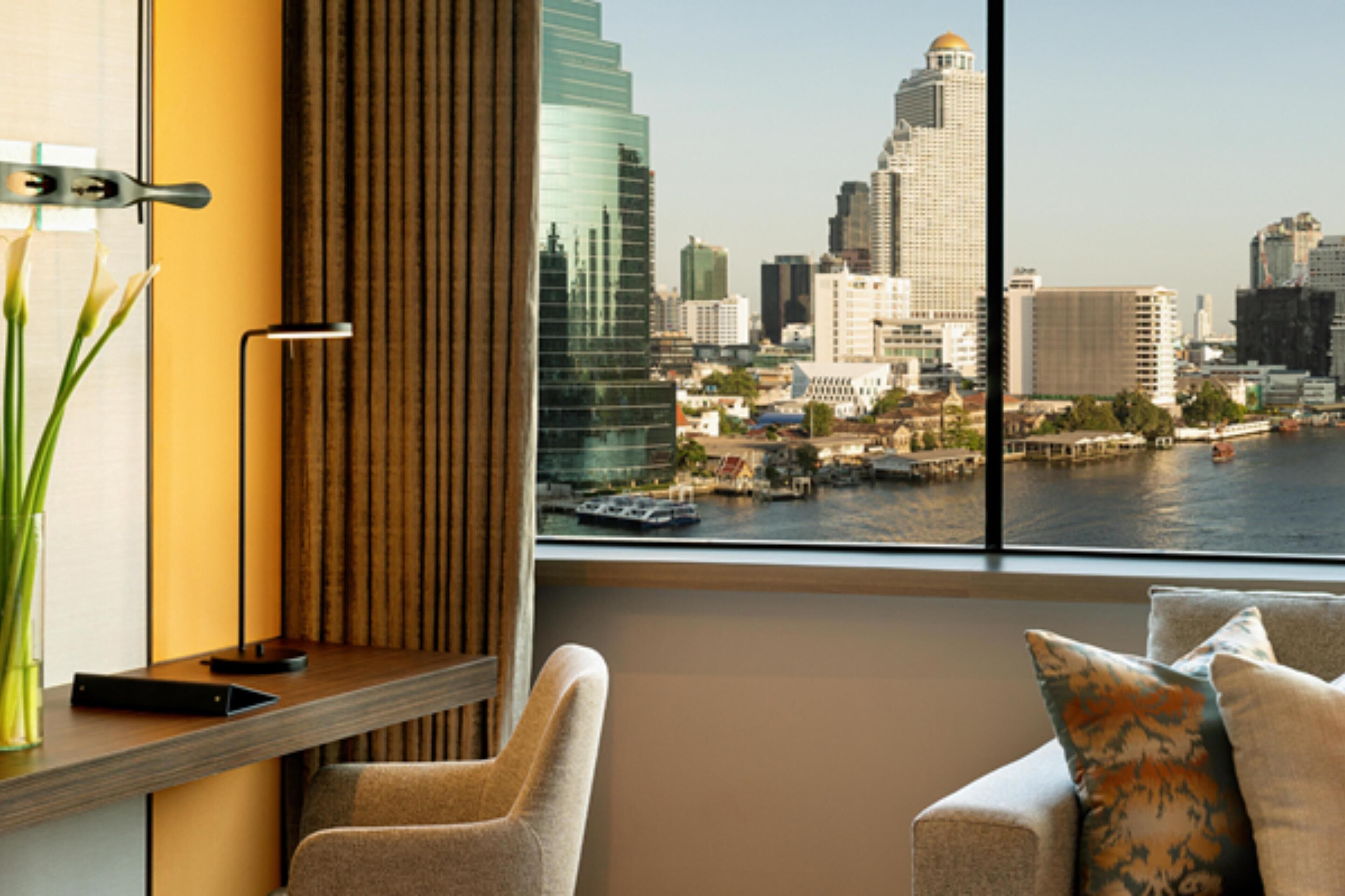 A modern hotel room with a view of a city skyline and a river.