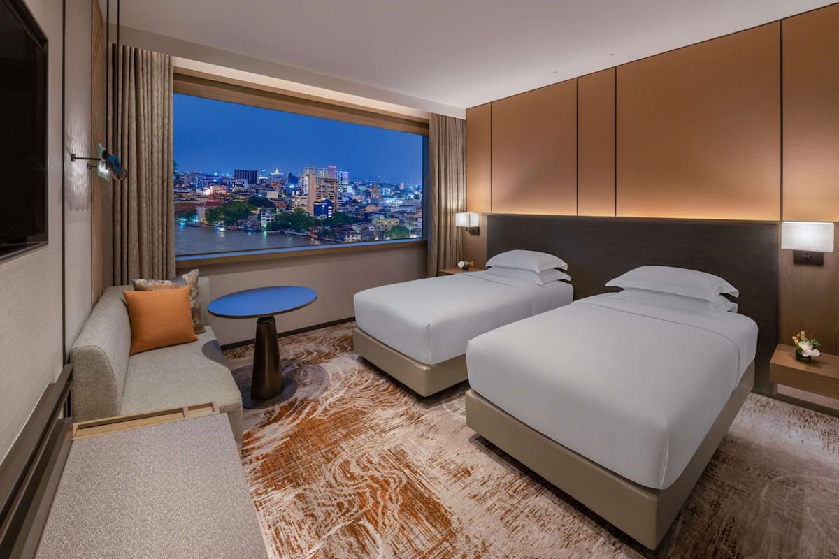 Habitación de hotel con vista a la ciudad, dos camas, un sofá, una mesita y un televisor.