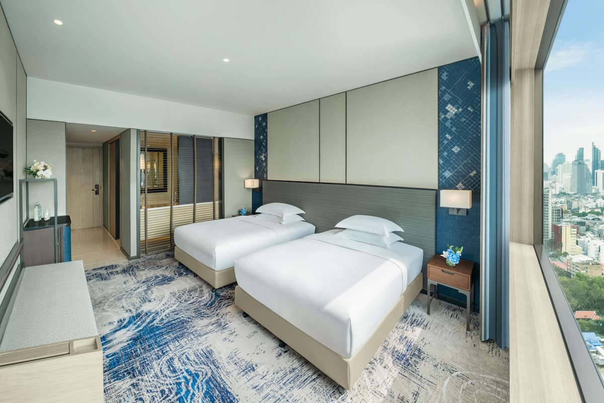 Una habitación de hotel moderna con dos camas, un escritorio y vista a la ciudad.