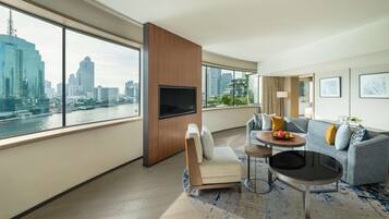 A modern hotel room with a large window offering a city view, a sofa, a small round table, and a TV mounted on a wooden panel.