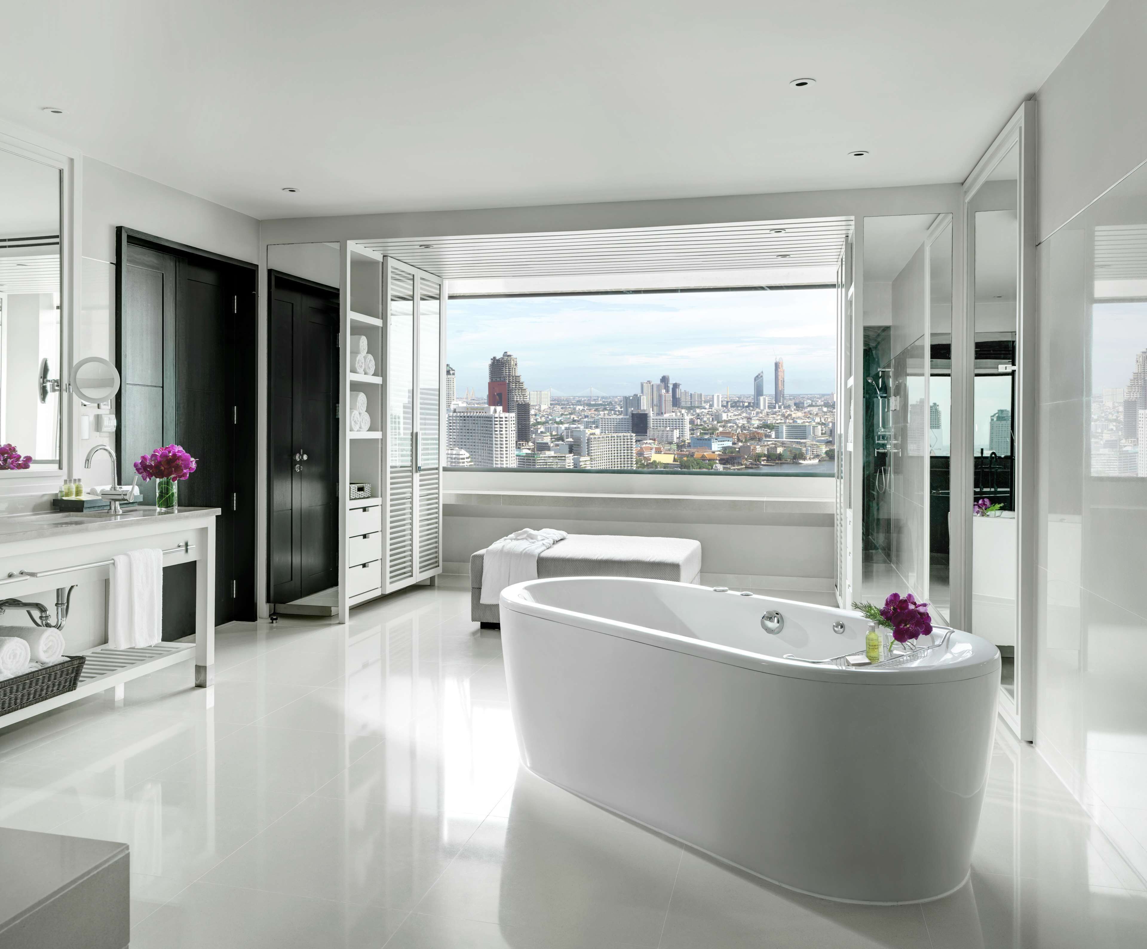 A modern bathroom with a freestanding bathtub, a vanity with a mirror, and a large window offering a city view.