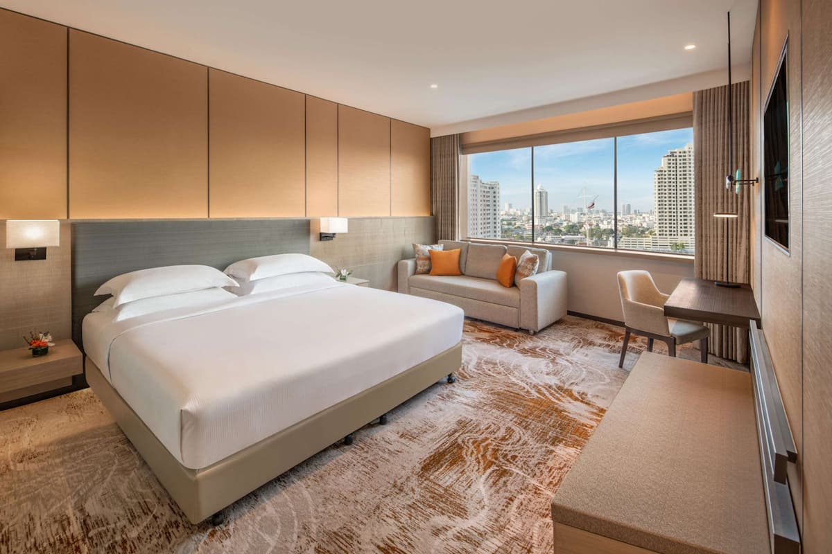 Una habitación de hotel moderna con una cama grande, un sofá, un escritorio y vistas a la ciudad.